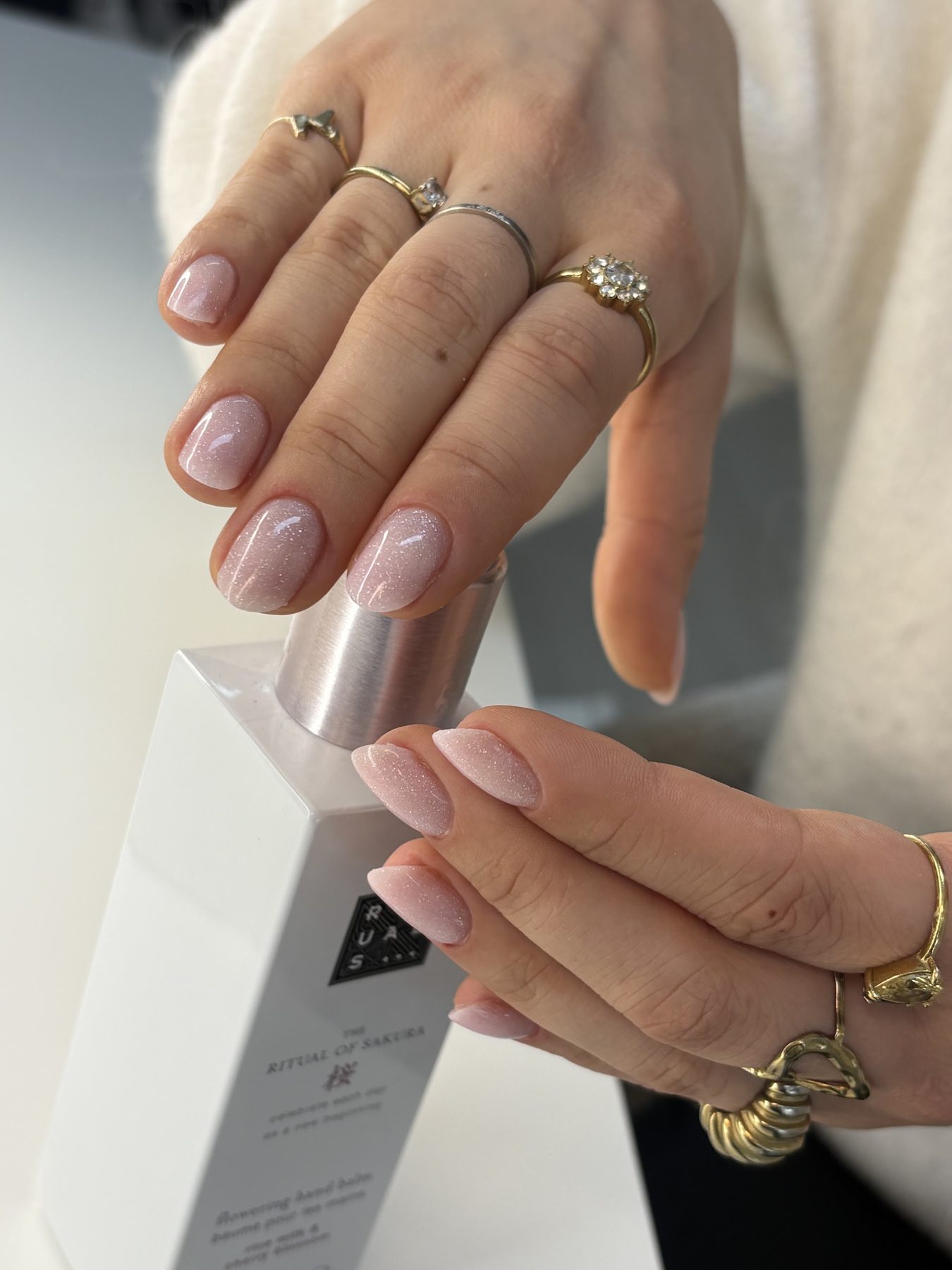 Nude nagels met shimmer, handen met gouden ringen